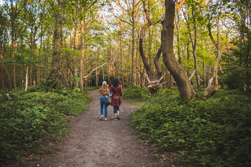 Teenage girl and her mother walking on footpath in park at sunset