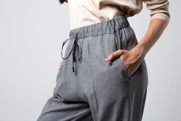 close-up of a young stylish girl in gray trousers standing with her hand in her pocket against a white wall.