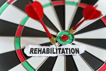 The picture shows a target, darts and a torn piece of paper with the inscription - REHABILITATION