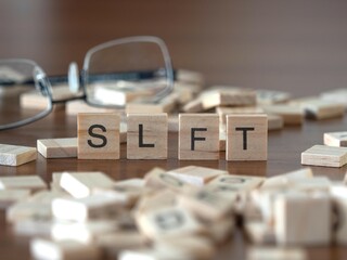 the acronym slft for scottish landfill tax word or concept represented by wooden letter tiles on a wooden table with glasses and a book