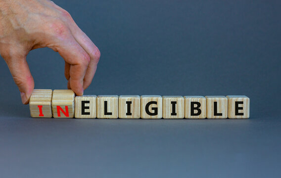 Eligible or ineligible symbol. Businessman turns wooden cubes and changes words Ineligible to Eligible. Beautiful grey table grey background. Business eligible or ineligible concept. Copy space.