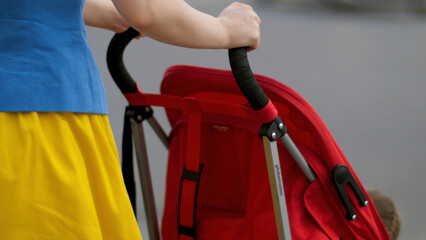 Young mother walking with baby carriage at the street back view close up. Mother with a stroller walks down the street