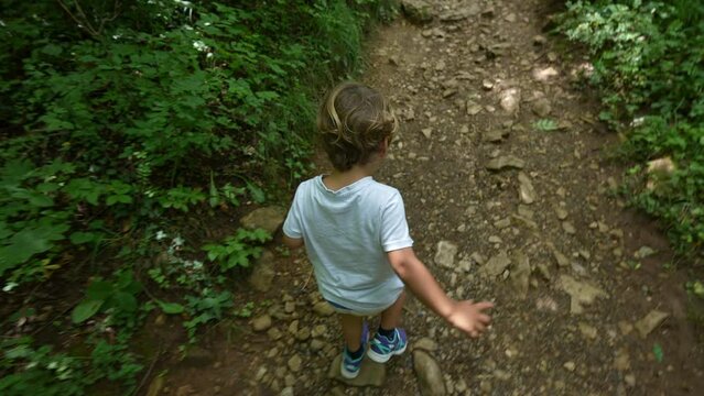 Child running in nature green path from above angle of little sportive boy in the woods hiking