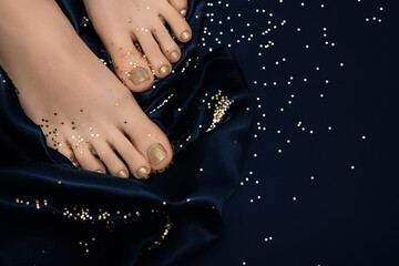 Female feet with golden pedicure. Woman legs with glitter golden nail design on blue fabric with...