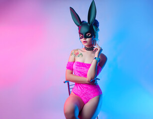 a girl in a bright pink bodysuit and a rabbit mask poses on a bright background of neon shades