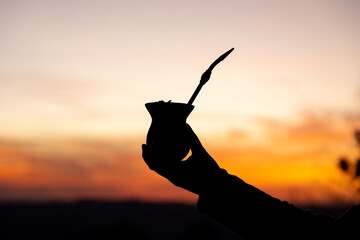 Silhouette of a hand holding a yerba mate gourd drink at sunset. Traditional South American drink....