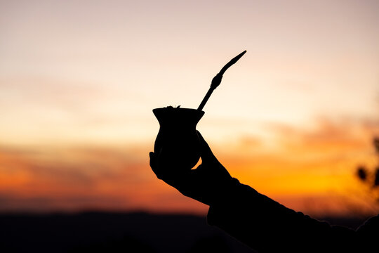Silhouette of a hand holding a yerba mate gourd drink at sunset. Traditional South American drink. Twilight sky