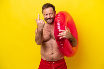 Middle age caucasian man holding inflatable donut isolated on yellow background doing coming gesture