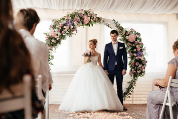 The bride and groom stand near the arch of roses at the wedding ceremony.