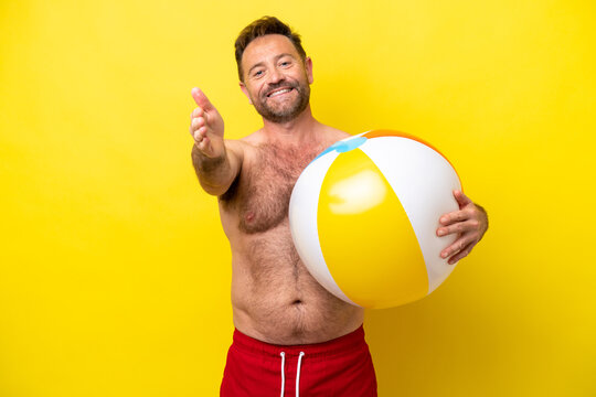 Middle age caucasian man holding beach ball isolated on yellow background shaking hands for closing a good deal