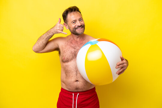 Middle age caucasian man holding beach ball isolated on yellow background making phone gesture. Call me back sign