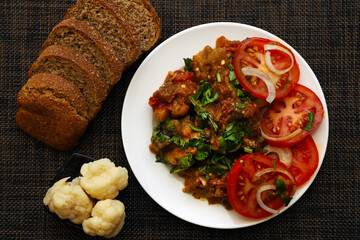 Salad of stewed vegetables with fresh herbs. A dish of eggplant caviar with salted cauliflower and brown bread on the table