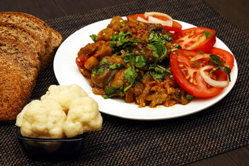 Salad of stewed vegetables with fresh herbs. A dish of eggplant caviar with salted cauliflower and brown bread on the table