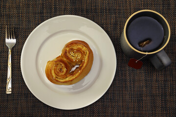 Roll with cinnamon and sesame seeds on a white plate with a mug of tea. View from above