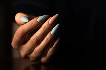 Wanddecoratie Nagelstudio Girl's hand with a beautiful light turquoise and beige manicure on the dark background, blank space  © nika57