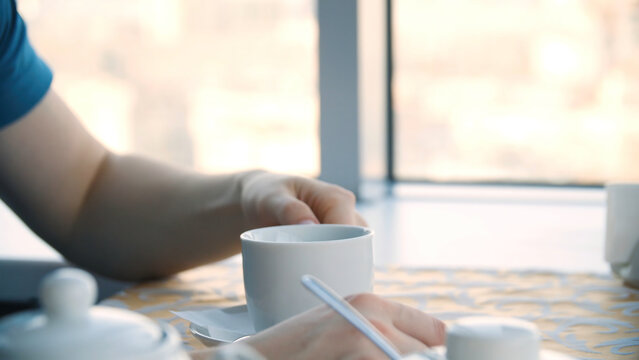 Close up of a hand of man holding a coffee cup beside a window. Young man drinking coffee in a cafe in front of the window