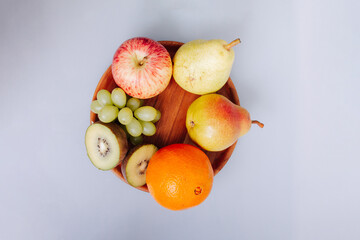  Assortment of fruits on a wooden plate and white background.