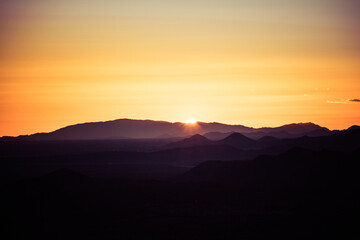 The sun setting behind the mountains of the Sonoran Desert in Arizona with the air lit up in golden light with mountains in silhouette.