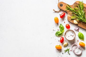 Food cooking background on white stone table. Fresh vegetables, herbs and spices with wooden cutting board. Top view with space for text.