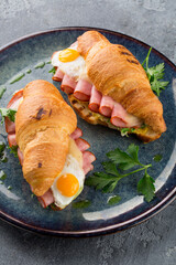 Crusty breakfast croissant sandwich with fried eggs and ham on a blue plate