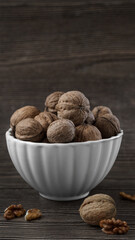 a white clay bowl filled with walnuts in the shell stands on a wooden background close-up. the concept of an organic harvest from his garden, preparation for winter, the last harvest.