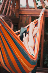 young woman relaxing in colorful hammock and using smartphone