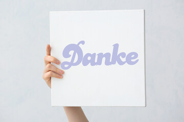 Female hand holding paper with word DANKE (German for Thanks) on light background