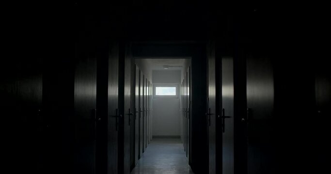 Camera movement dark corridor with prison doors. Door handles with locks. At the end of the tunnel there is a bright window, glare of light in the doors.
