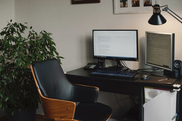 Freelancer workspace, home working place with computer and screen. Comfortable desk without people with home plant and lamp. Boho vintage chair by the window
