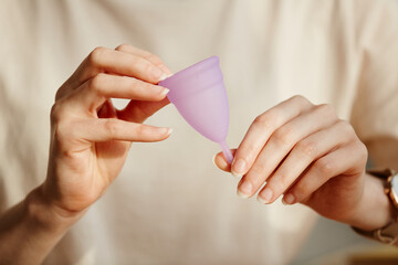 Minimal closeup of young woman holding pink menstrual cup and showing it to camera, copy space