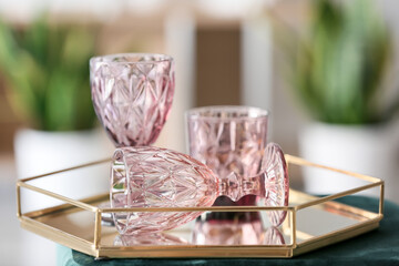Tray with stylish empty glasses on pouf in light room