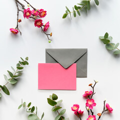 Red plum flowers on twigs, fresh eucalyptus leaves. Blank pink card with grey envelope. Copy-space,...