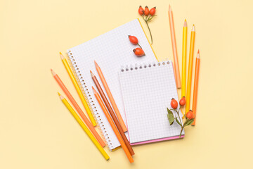 Notebooks with colorful pencils and rose hip berries on color background