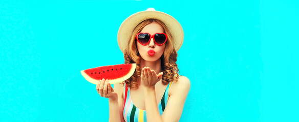 Summer portrait of beautiful young woman blowing her lips with red lipstick sending air kiss with slice of watermelon wearing straw hat on blue background, blank copy space for advertising text