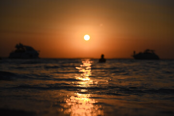 Caribbean beach sunset, with the sun setting on the horizon, with a boat sailing along the beach