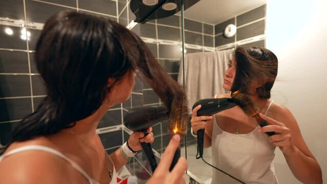 Woman drying and combing hair in front of mirror