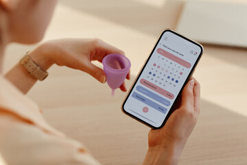 Close up of young woman calculating menstrual cycle using mobile app calendar, copy space