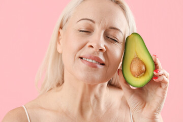 Mature blonde woman with avocado on pink background, closeup