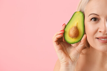 Mature blonde woman with avocado on pink background, closeup