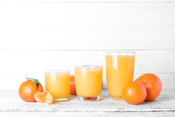 Glasses of delicious tangerine juice on white wooden background