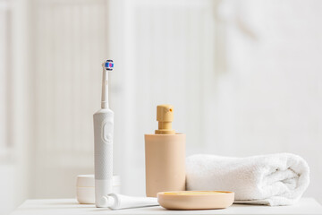 Fototapeta na wymiar Electric toothbrush, cosmetic products and rolled towel on table
