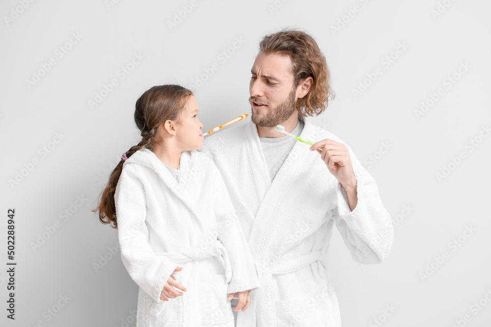 Wall mural Little girl with her father brushing teeth on light background