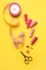Thread spools, ribbon, safety pin and scissors on yellow background