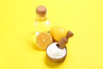 Bottle of water, ripe lemon and bowl of baking soda on yellow background