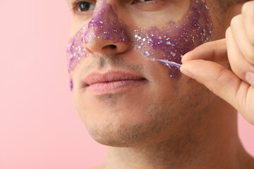 Handsome man with glitter mask on pink background, closeup