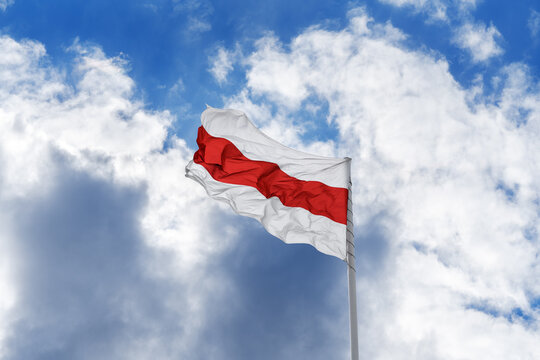 The flag of protests in Belarus 2020. White-red-white historical flag of Republic of Belarus is waving in front of blue sky and clouds.