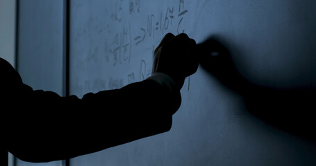 Scientist writing formulas on chalkboard. Hand with chalk wrote physics formulas on black chalkboard closeup