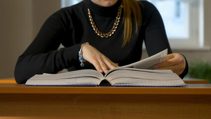 Women's hands leafing through a book. Woman sitting at the table leafing through the book