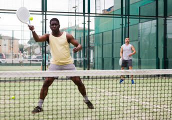 Obraz premium African american man and his partner playing paddle tennis on the padel court