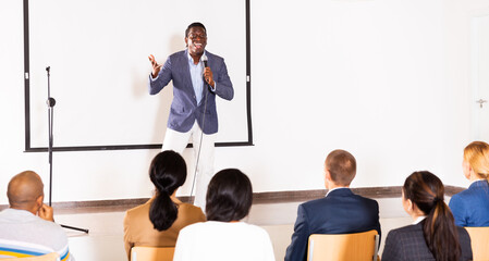 Emotional aframerican business coach giving motivational training for group of businesspeople, speaking from stage in conference room